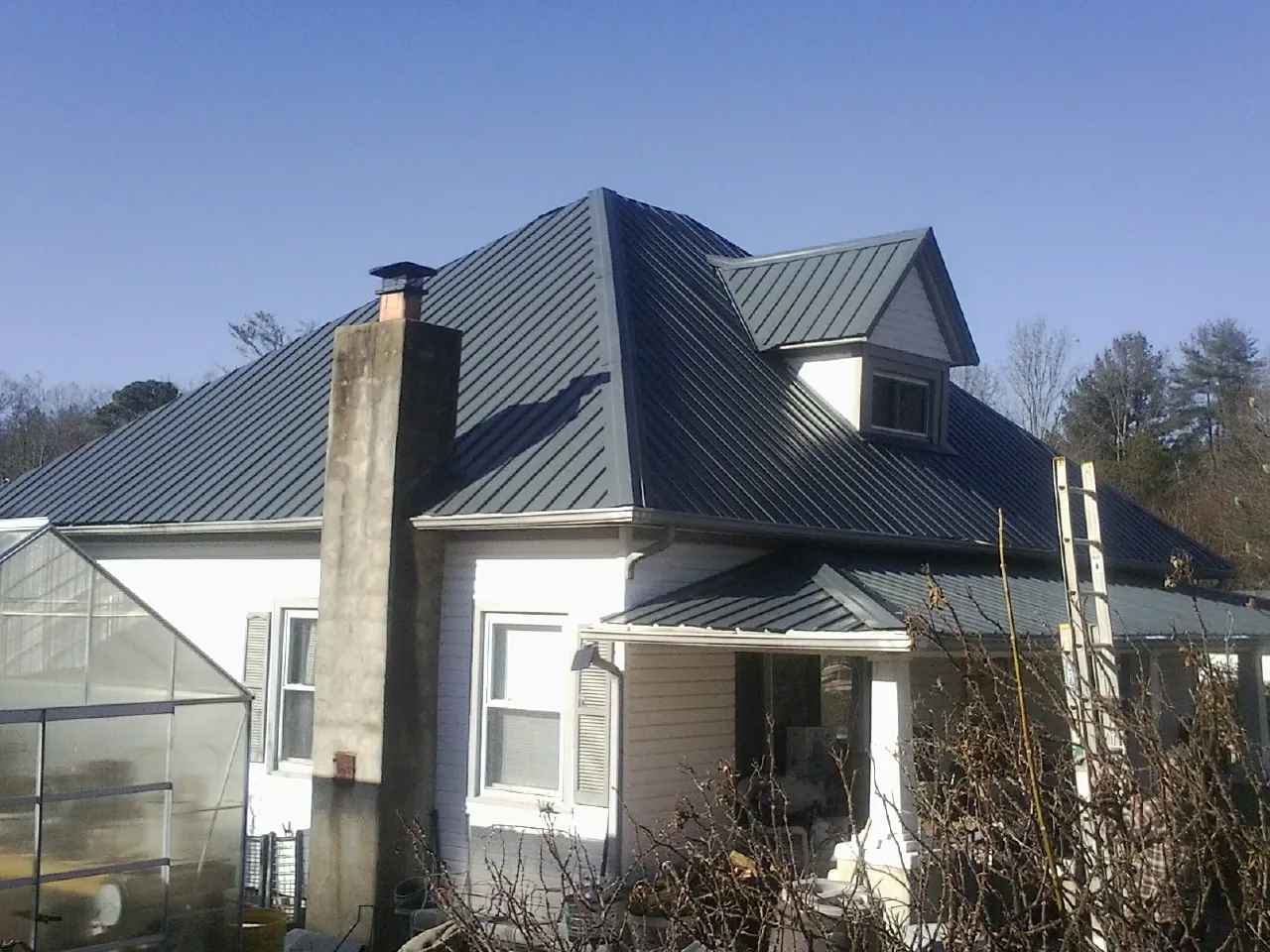 Dark blue standing seam metal roof on a white farmhouse with dormer — Slate & Tile Roof Repair by Roofing Brothers in Gallion