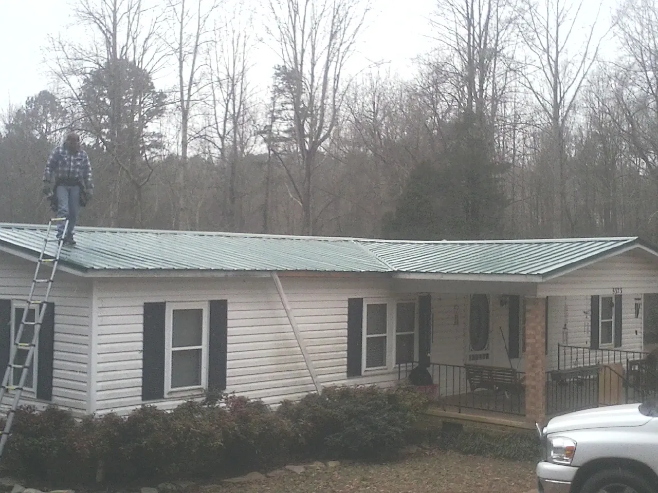 Worker on a ladder beside a new green metal roof on a ranch home in Gallion
