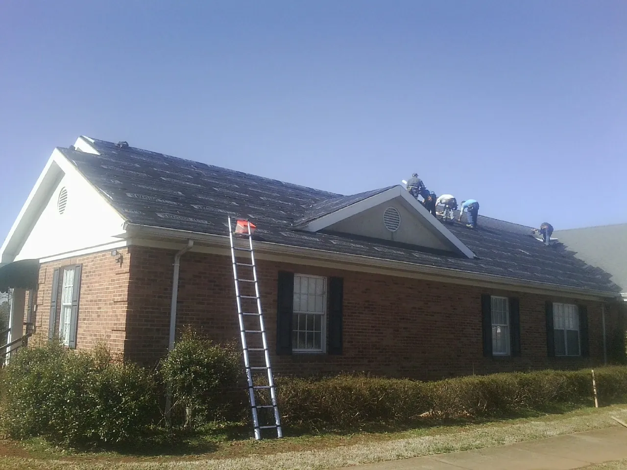 Crew tearing shingles off a brick ranch roof with a ladder set — Emergency Roof Repair work by our crew in Gallion