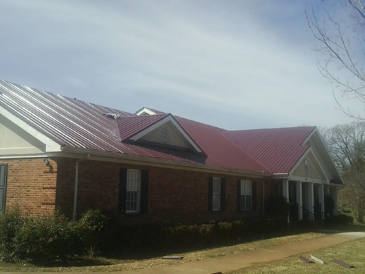 Red metal roof with gabled entries on a long brick building, from a Hail Damage Roof Repair job in Gallion