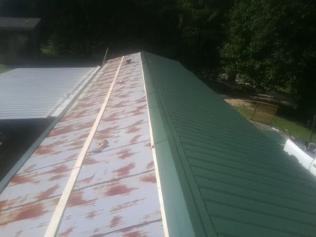 Old rusted panels beside newly installed green metal roofing — Wind Damage Roof Repair by Roofing Brothers in Gallion