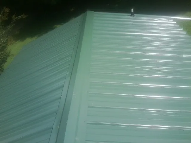 New green metal panels meeting at the ridge of a roof — Flat Roof Repair work by our crew in Gallion
