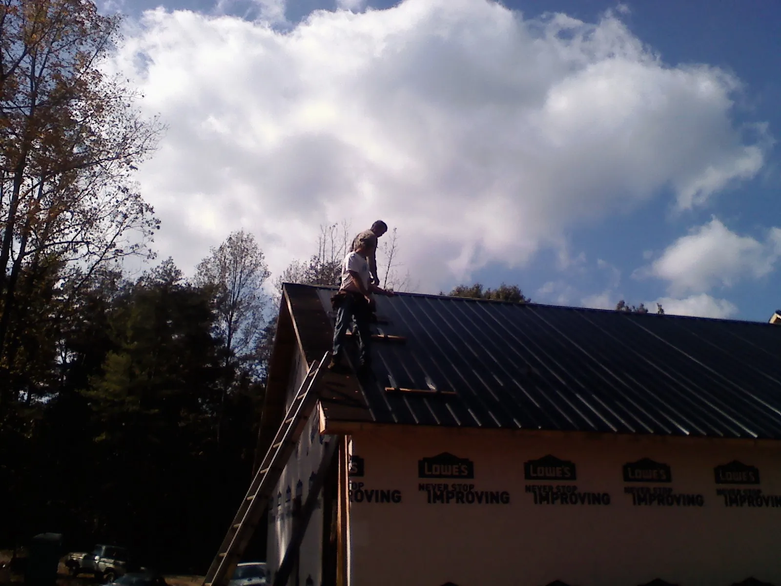 Roofer fastening dark metal panels high against a cloudy sky, from a Roof Inspection job in Gallion