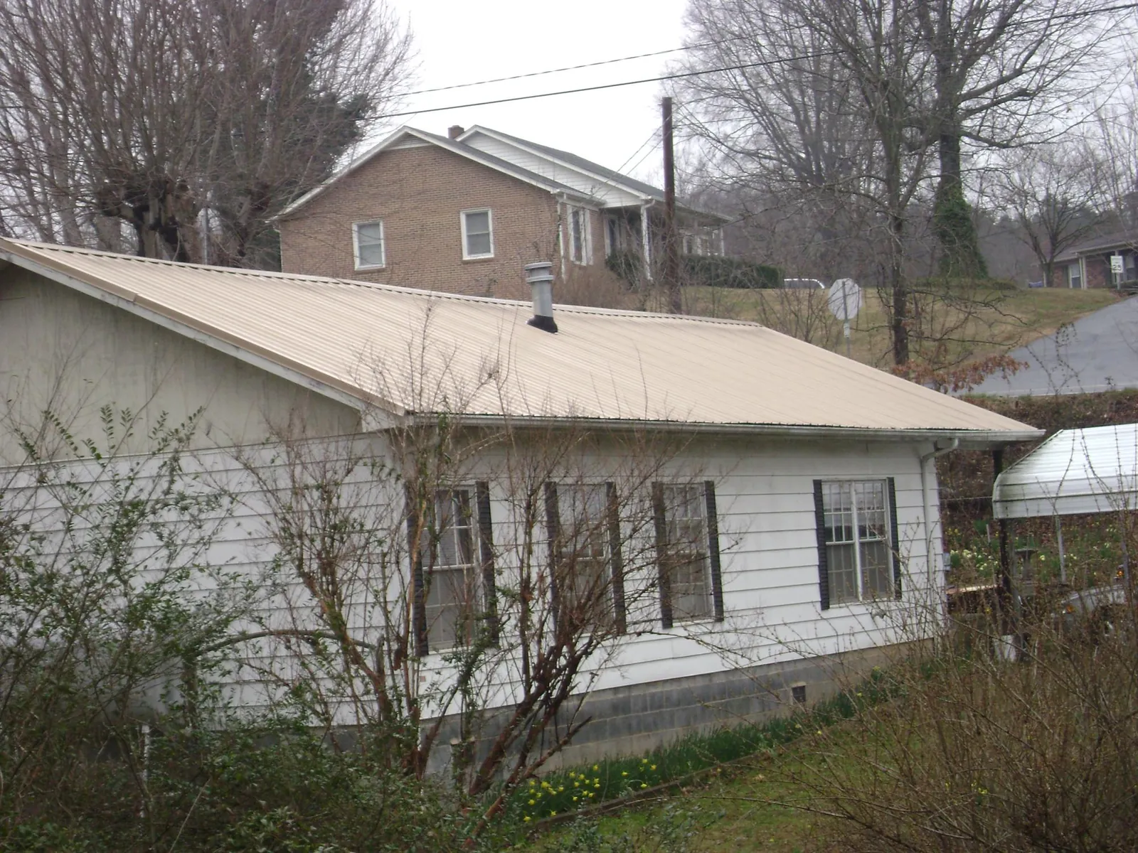 Tan metal roof on a white sided house set into a hillside — Commercial Roofing by Roofing Brothers in Gallion