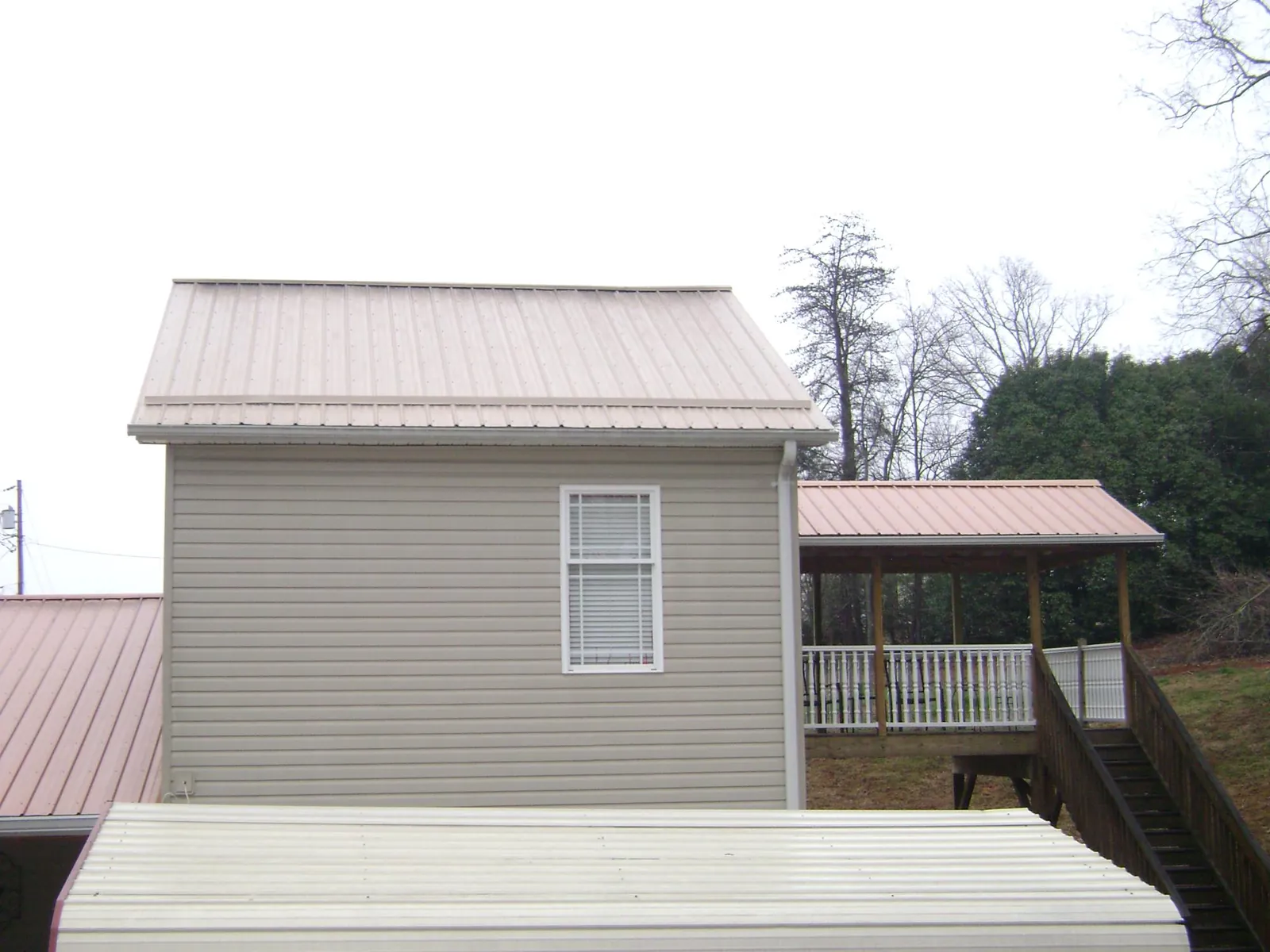 Tan metal roofs on a two story addition and attached porch, from a Roof Replacement job in Gallion